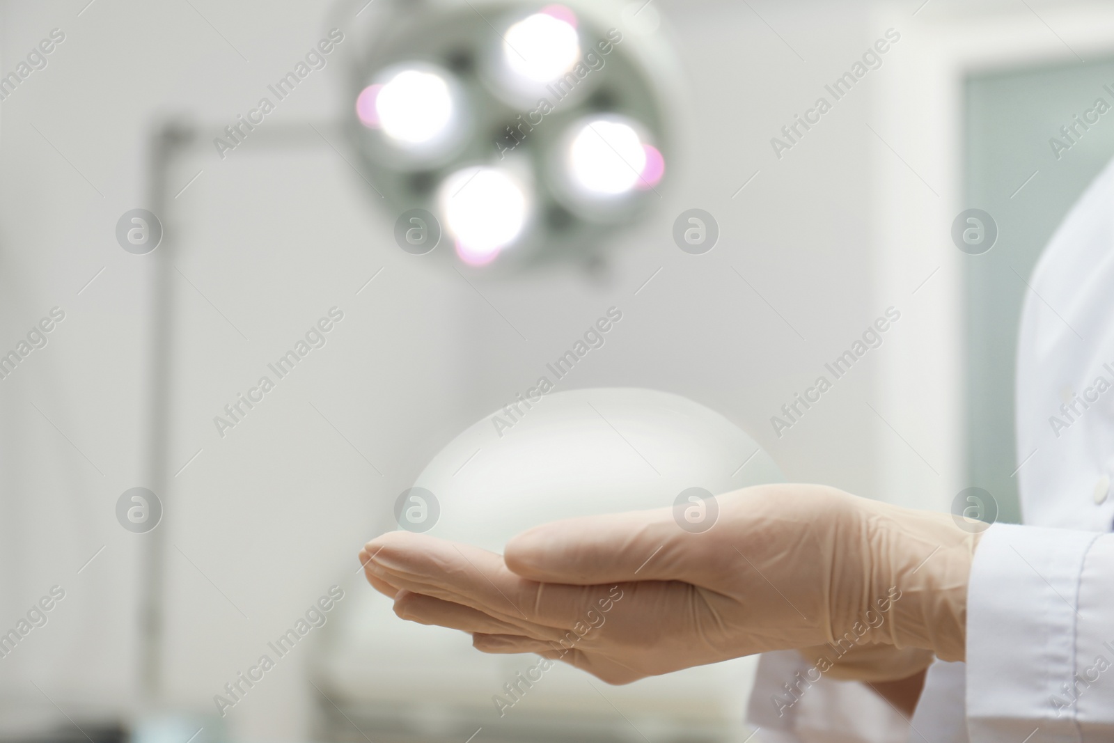 Photo of Doctor holding silicone implant for breast augmentation in clinic, closeup with space for text. Cosmetic surgery