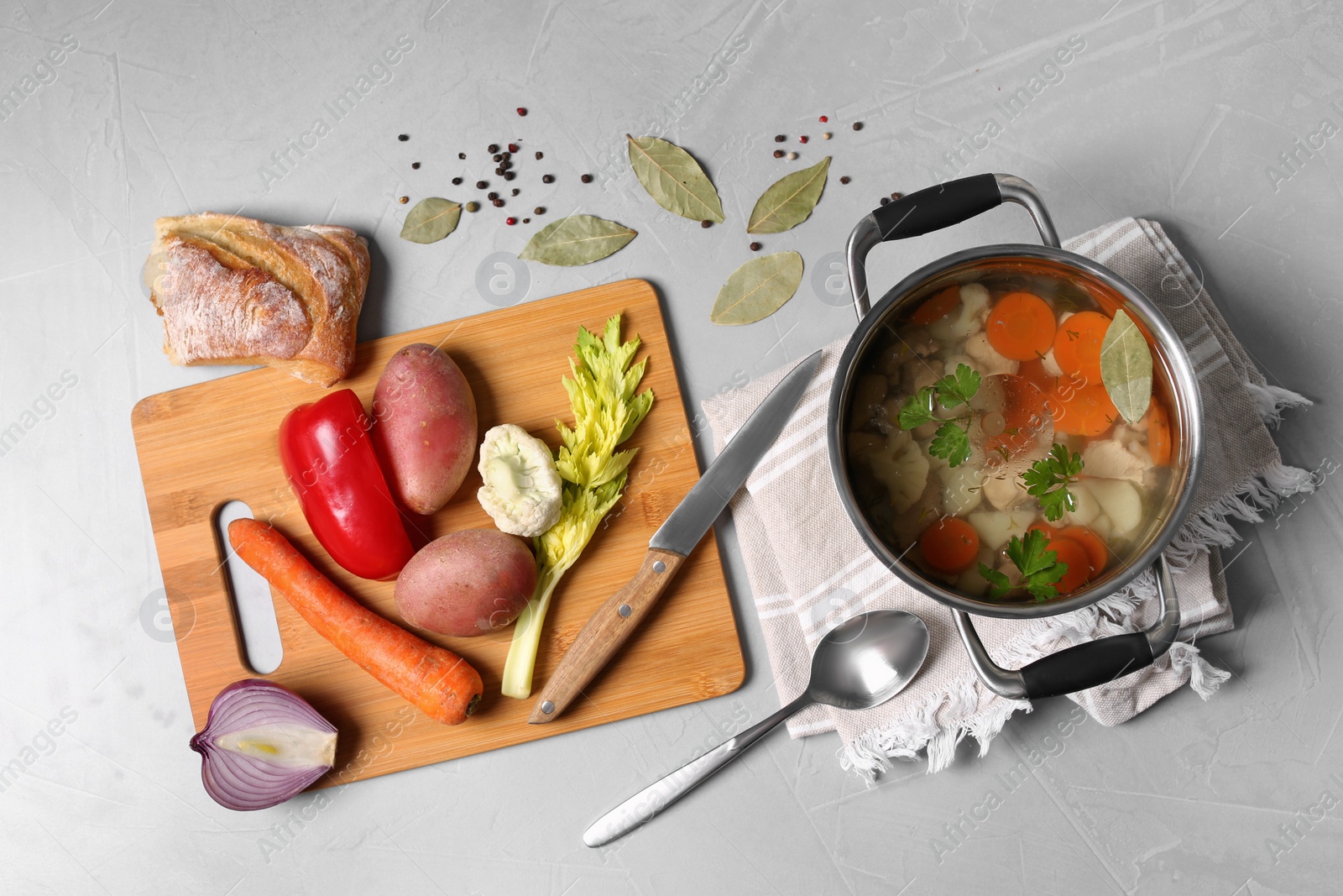 Photo of Pot of delicious vegetable bouillon and ingredients on light grey table, flat lay