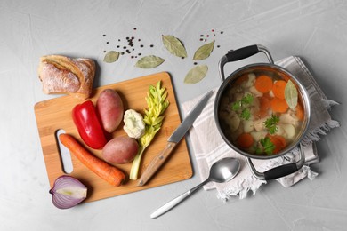 Pot of delicious vegetable bouillon and ingredients on light grey table, flat lay