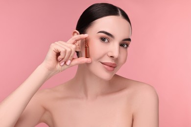 Beautiful young woman holding skincare ampoule on pink background