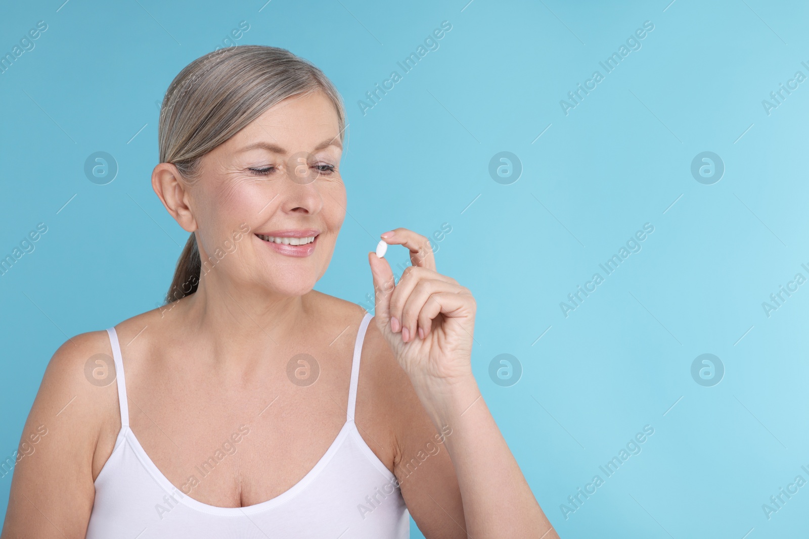 Photo of Beautiful woman with vitamin pill on light blue background, space for text