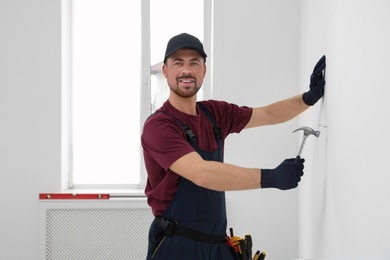 Photo of Handyman in uniform working with hammer indoors. Professional construction tools