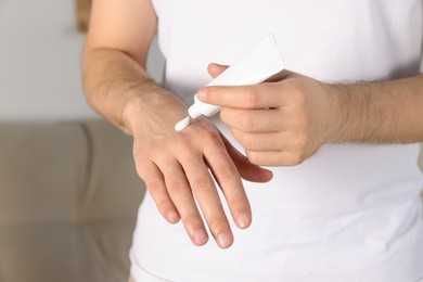 Photo of Man applying cream onto hand at home, closeup