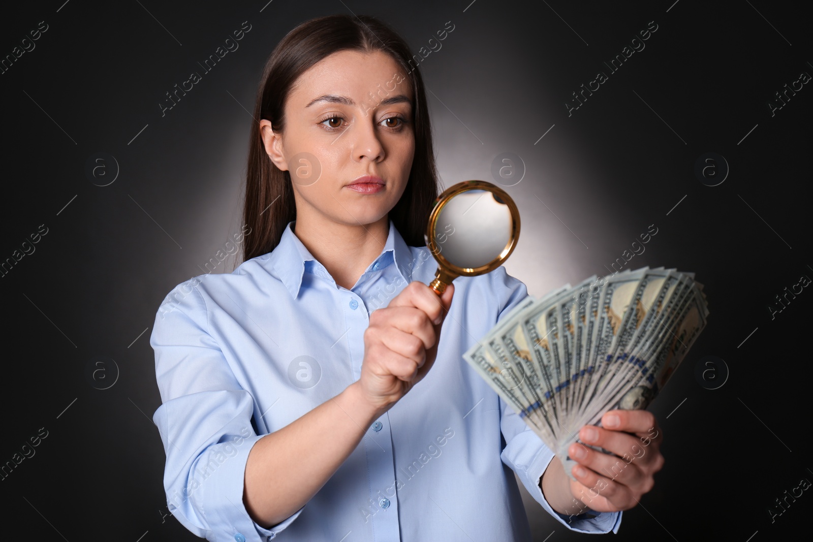 Photo of Expert authenticating 100 dollar banknotes with magnifying glass against dark background. Fake money concept