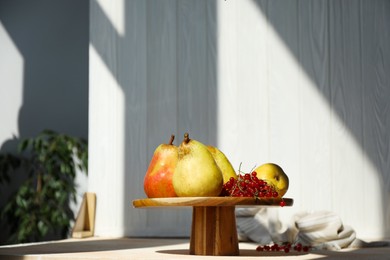 Photo of Stand with juicy pears, red currants and double-sided backdrop in photo studio