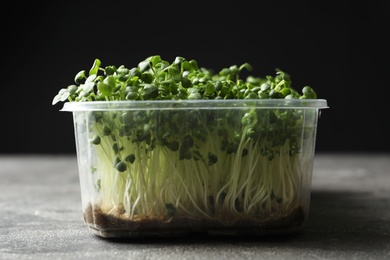 Photo of Sprouted arugula seeds in plastic container on grey table, closeup
