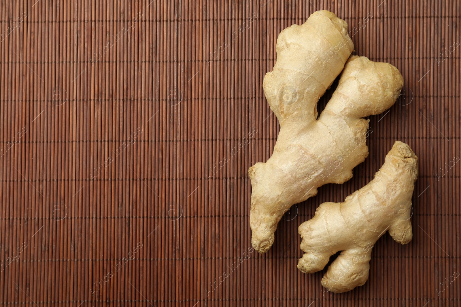 Photo of Fresh ginger on bamboo mat, top view. Space for text