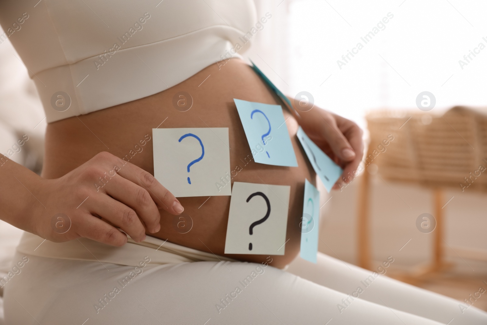 Photo of Pregnant woman with sticky notes on belly indoors, closeup. Choosing baby name