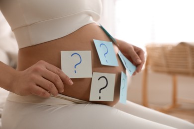 Pregnant woman with sticky notes on belly indoors, closeup. Choosing baby name
