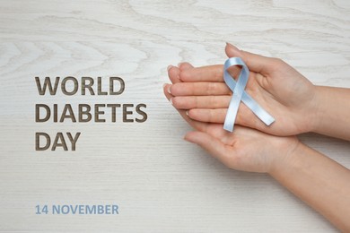 Image of World Diabetes Day. Woman with light blue awareness ribbon at wooden table, closeup