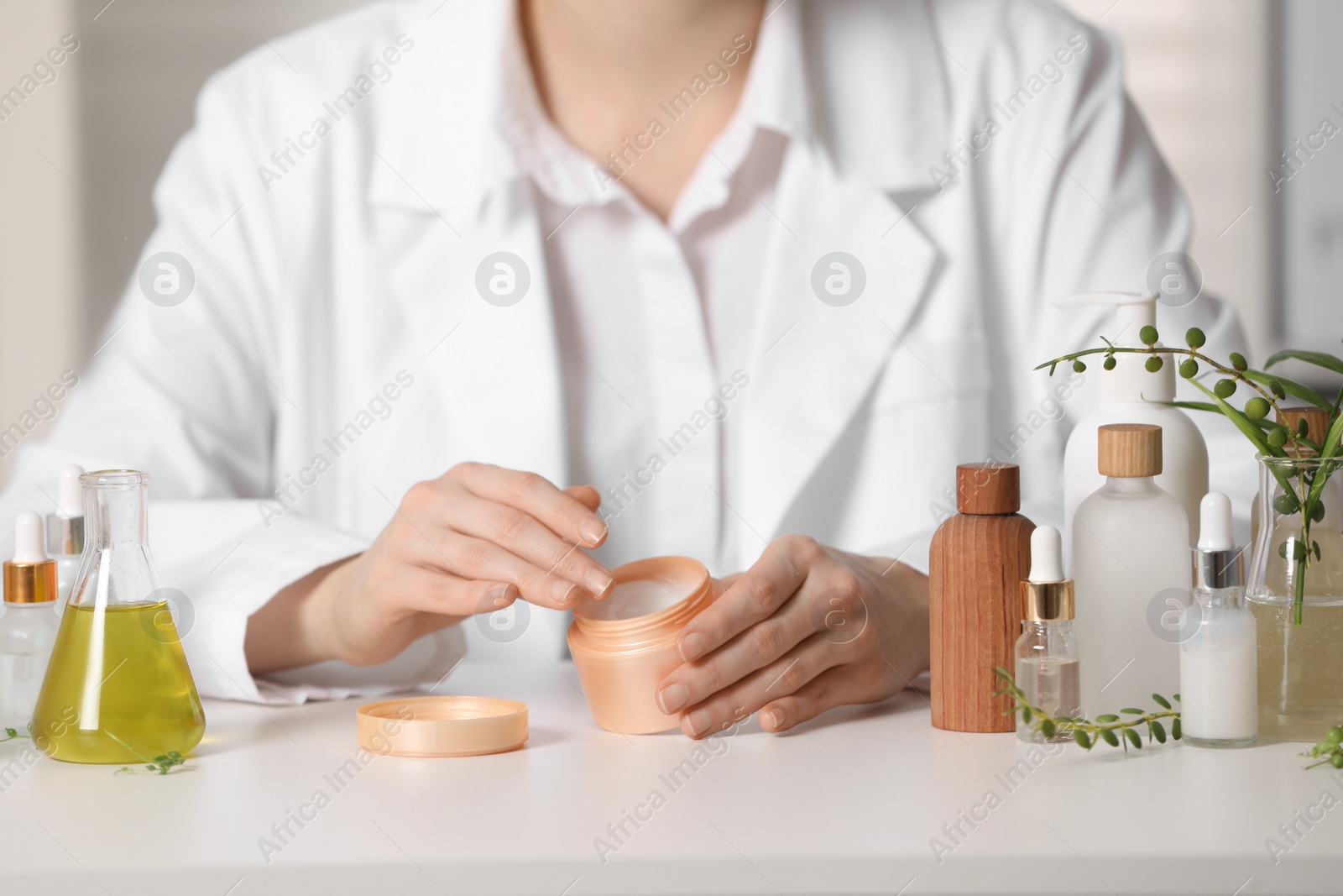 Photo of Dermatologist with jar testing cosmetic product at white table indoors, selective focus