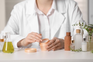 Photo of Dermatologist with jar testing cosmetic product at white table indoors, selective focus