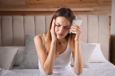 Woman holding glass of medicine for hangover on bed at home