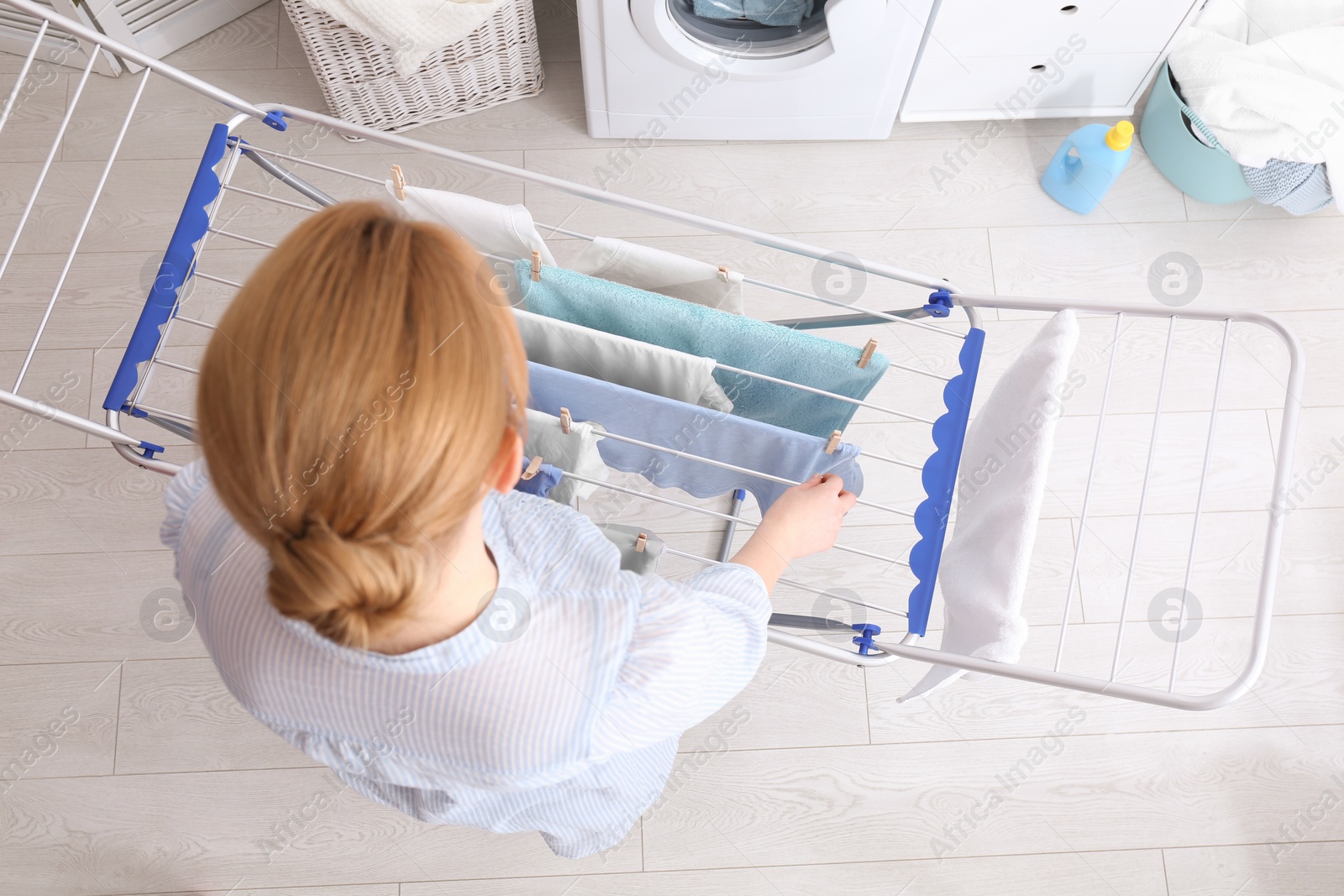 Photo of Woman hanging clean laundry on drying rack indoors, above view