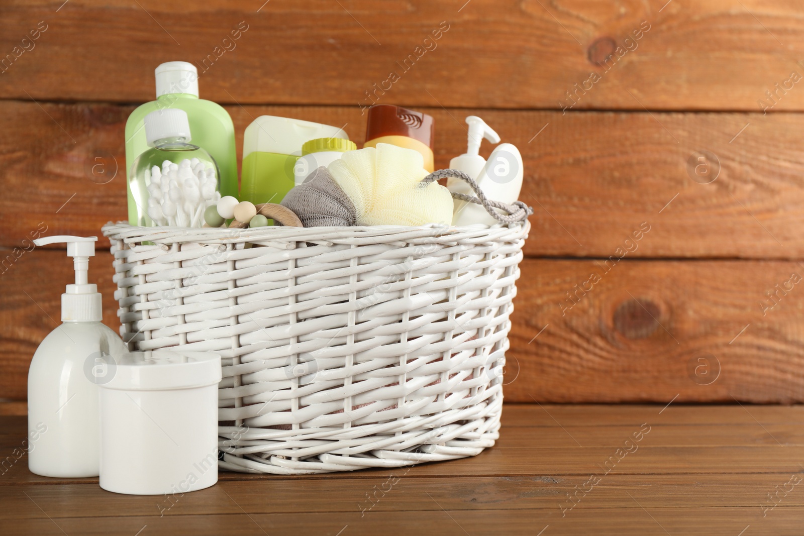 Photo of Wicker basket with different baby cosmetic products, accessories and toy on wooden table. Space for text