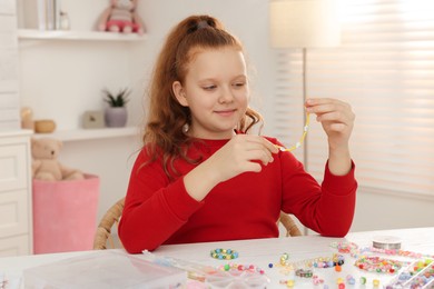 Photo of Cute girl making beaded jewelry at table in room