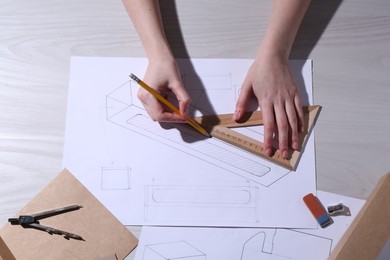 Woman creating packaging design at light wooden table, top view