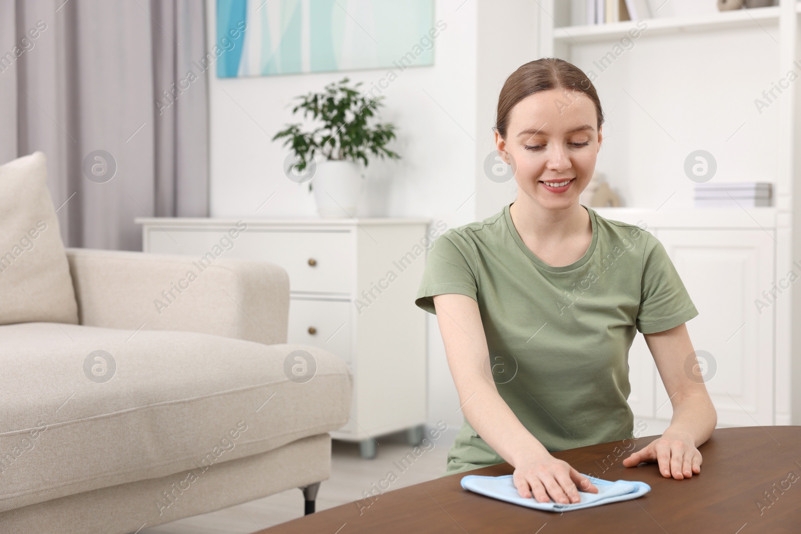 Photo of Woman with microfiber cloth cleaning wooden table in room