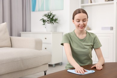 Woman with microfiber cloth cleaning wooden table in room