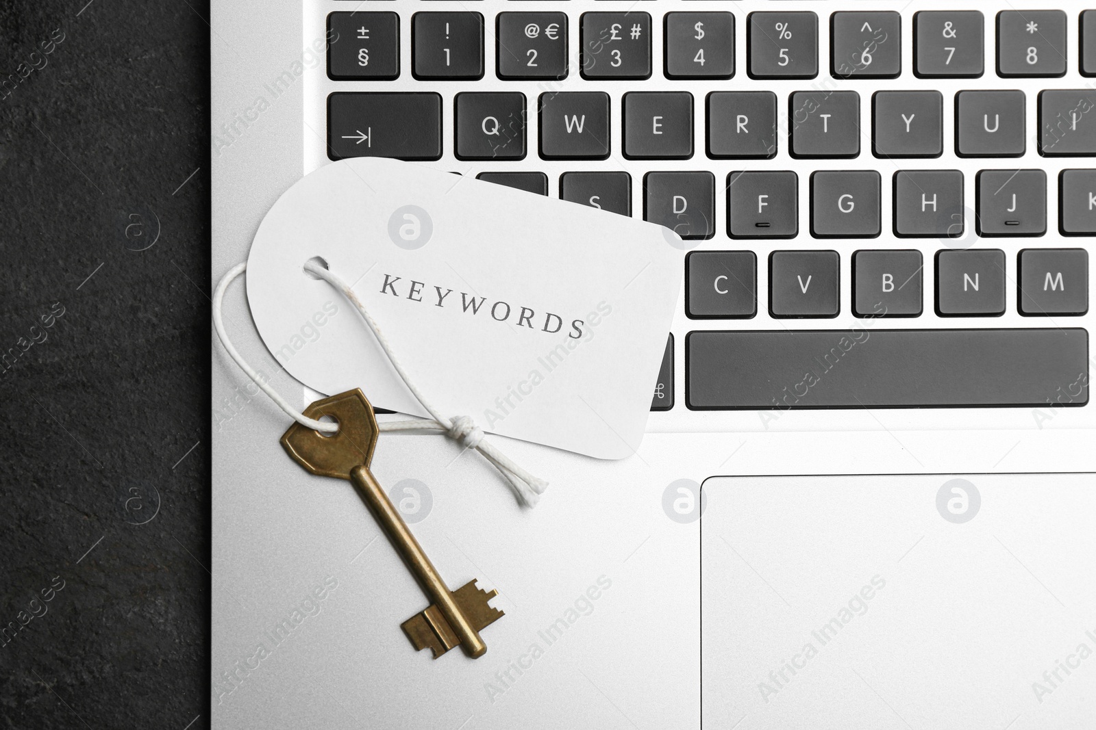 Photo of Laptop, key and tag with word KEYWORDS on black table, top view