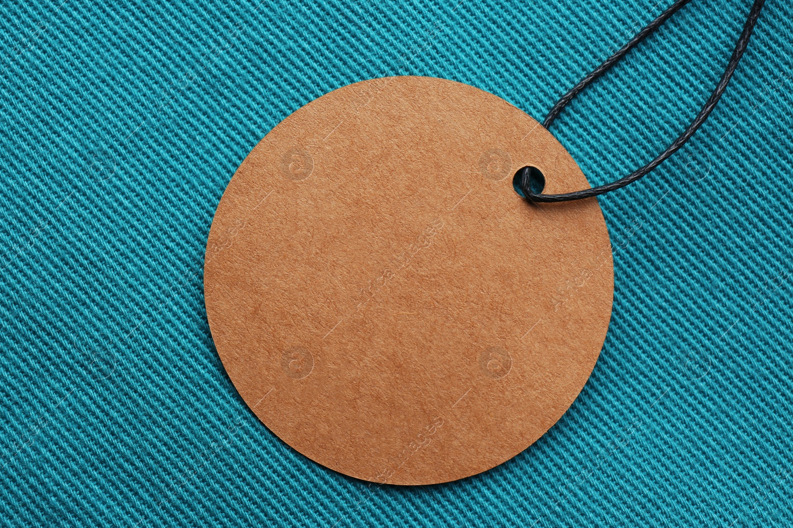 Photo of Circle shaped tag with space for text on dark turquoise fabric, top view