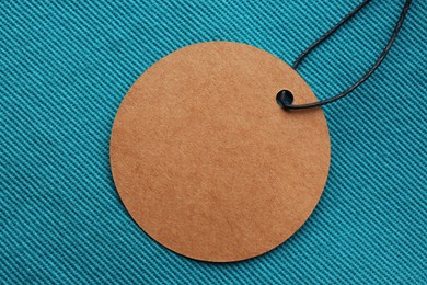 Photo of Circle shaped tag with space for text on dark turquoise fabric, top view