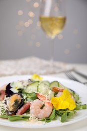 Plate of delicious salad with seafood on white table against blurred lights