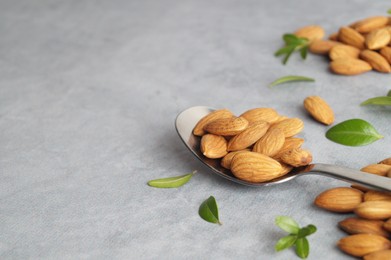 Photo of Spoon with tasty almonds and fresh green leaves on light grey table. Space for text