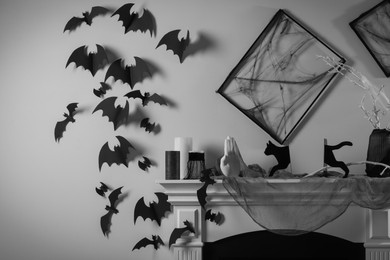 Black frames with cobweb on white wall, paper bats and different Halloween decor on fireplace indoors
