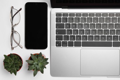 Modern laptop, houseplants, glasses and smartphone on white table, flat lay