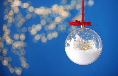 Decorative snow globe hanging against blurred festive lights, closeup. Space for text