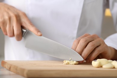 Photo of Professional chef cutting garlic at white marble table indoors, closeup