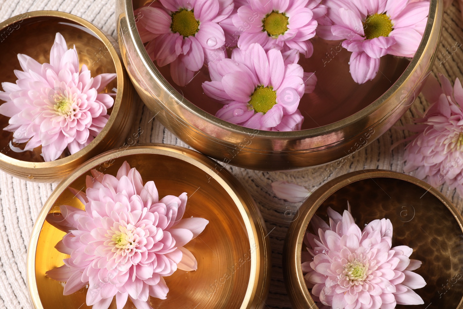 Photo of Tibetan singing bowls with water and beautiful flowers on table, flat lay