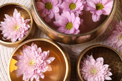 Tibetan singing bowls with water and beautiful flowers on table, flat lay