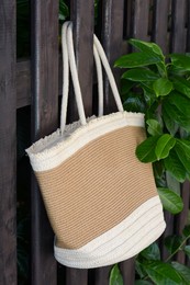 Photo of Stylish bag hanging on wooden fence outdoors. Beach accessory