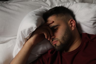 Photo of Sad man lying on bed at home, top view