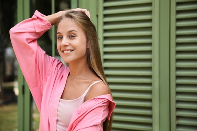 Beautiful young woman in stylish pink shirt near shutters, space for text