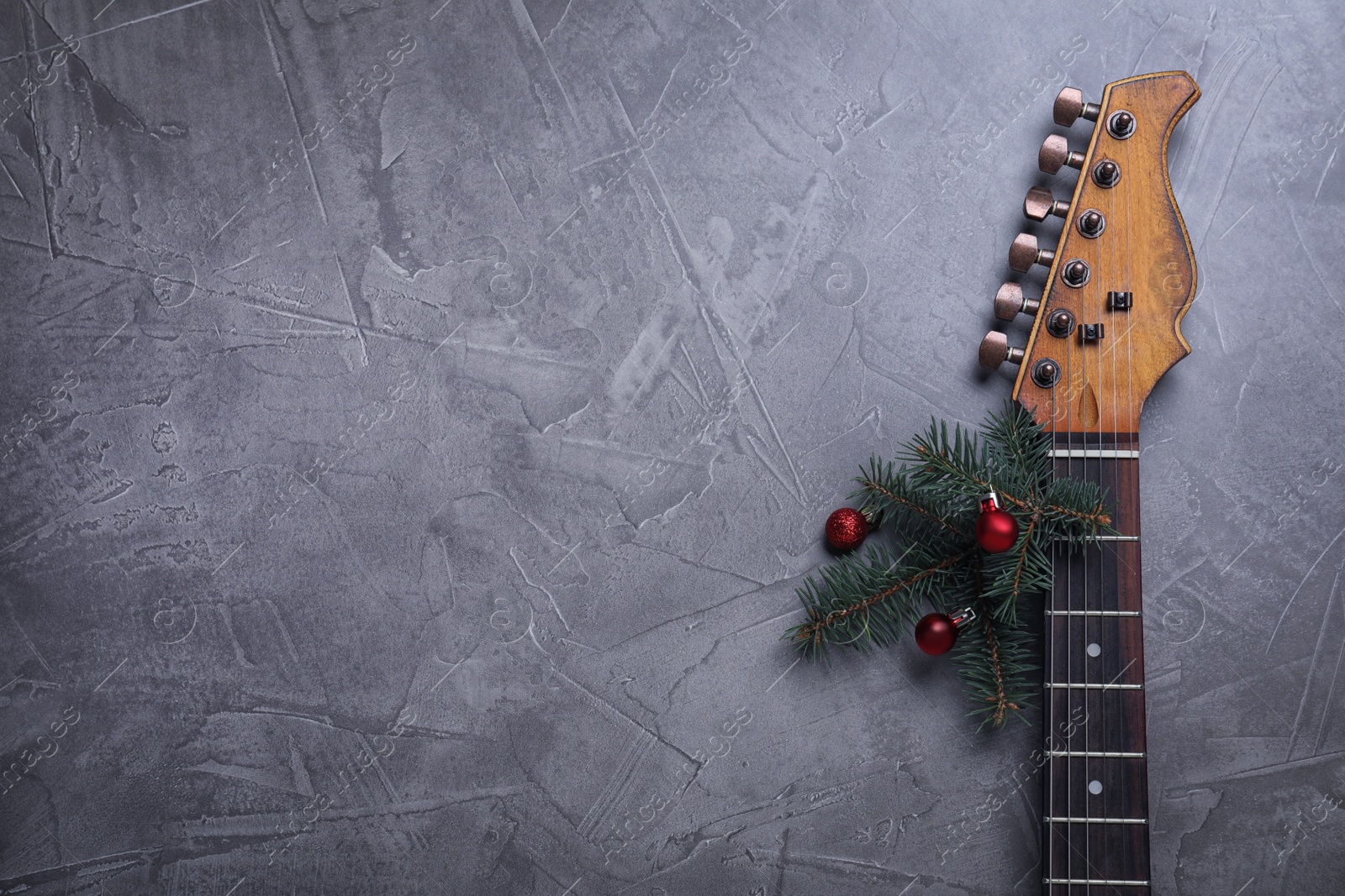 Photo of Guitar with fir tree branch and red baubles on grey background, space for text. Christmas music