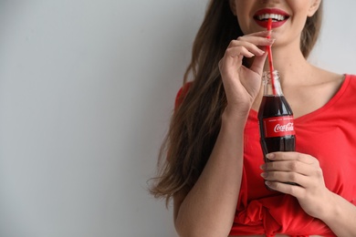 Photo of MYKOLAIV, UKRAINE - NOVEMBER 28, 2018: Young woman with bottle of Coca-Cola on white background, space for text