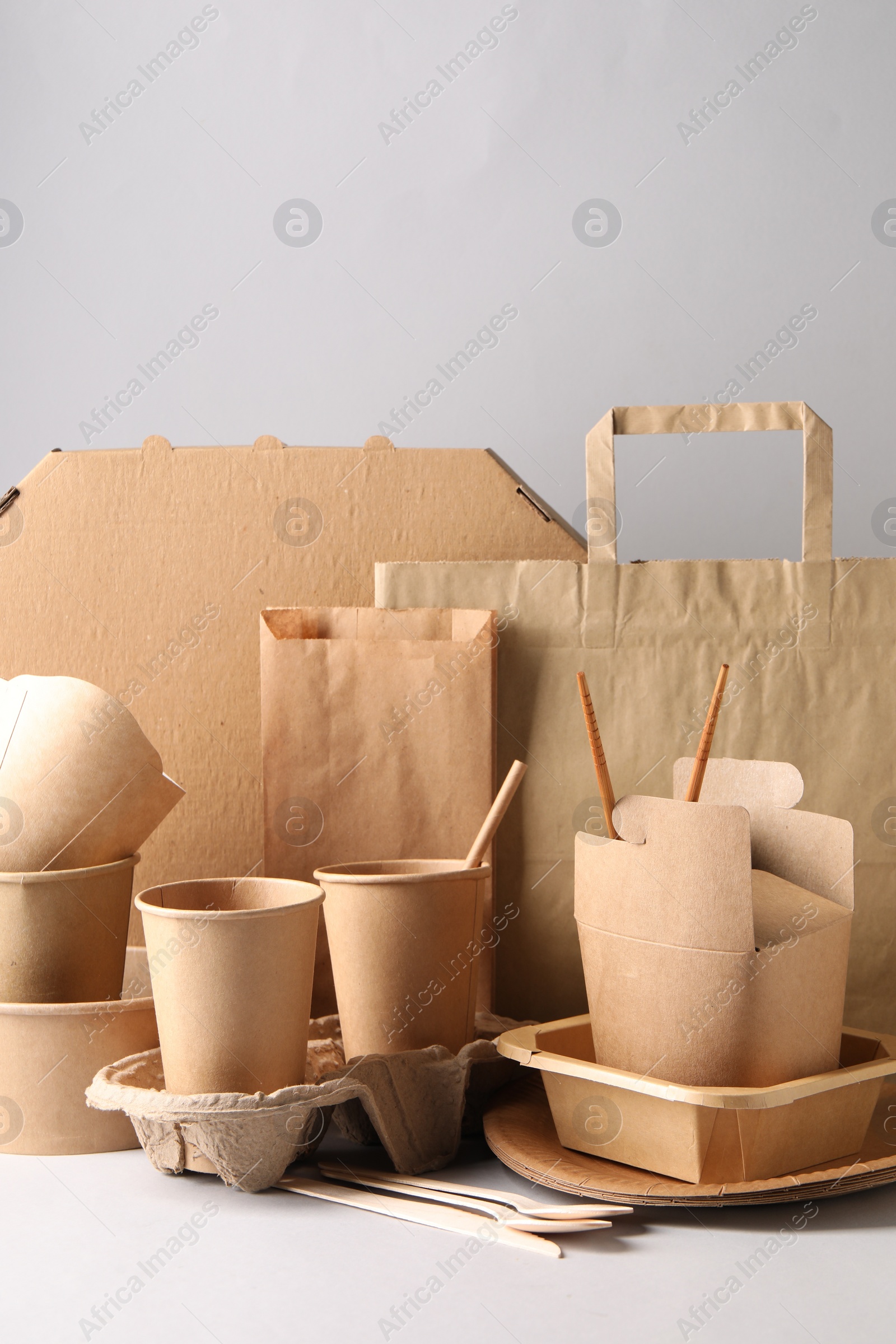 Photo of Eco friendly food packaging. Paper containers, tableware and bag on light background