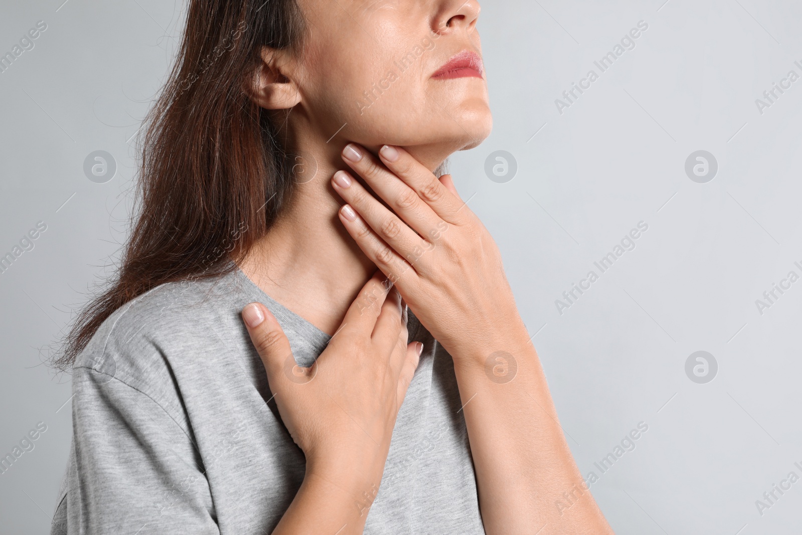 Photo of Mature woman doing thyroid self examination on light background, closeup
