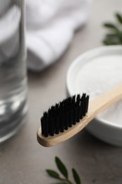 Bamboo toothbrush and bowl of baking soda on grey table, closeup