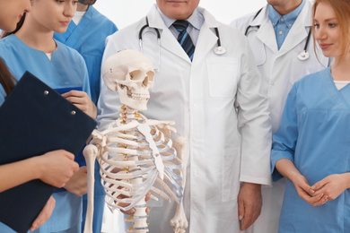 Photo of Professional orthopedist with human skeleton model teaching medical students, closeup