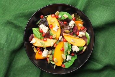 Photo of Delicious persimmon salad with pomegranate and spinach on dark green cloth
