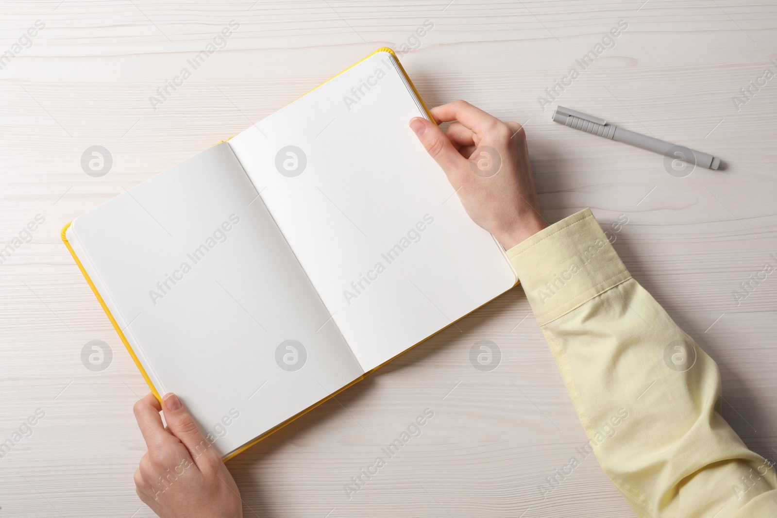 Photo of Woman holding open notebook at white wooden table, top view