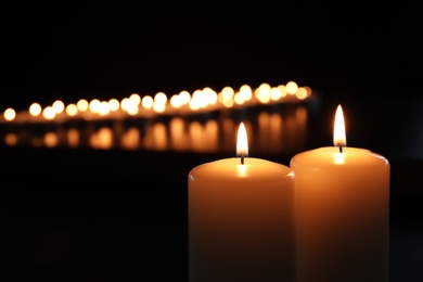 Photo of Small wax candles burning in darkness, closeup