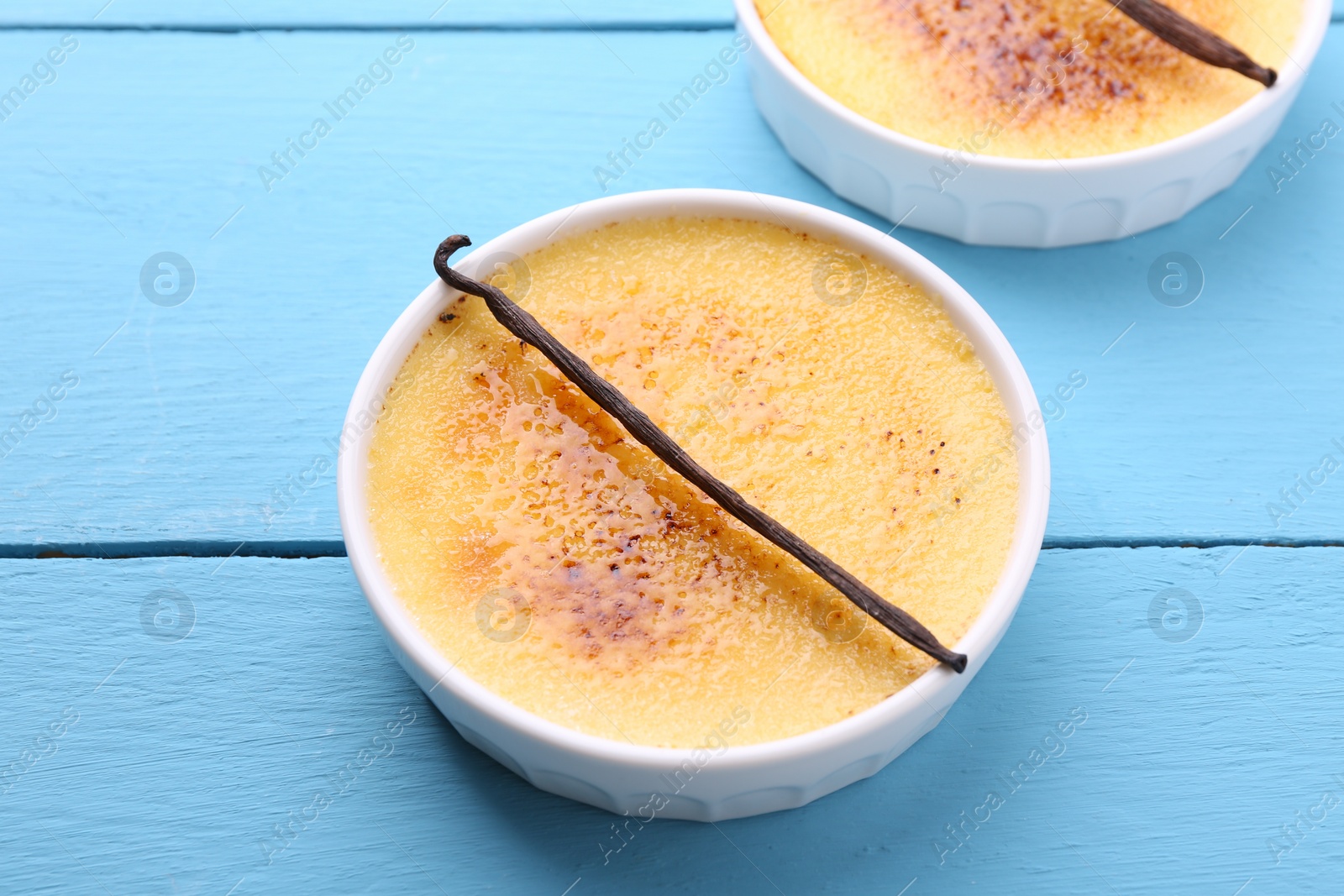 Photo of Delicious creme brulee in bowls and vanilla pods on light blue wooden table