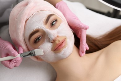 Photo of Cosmetologist applying mask on woman's face, top view