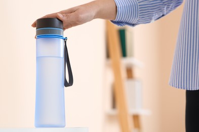 Woman taking bottle of water indoors, closeup