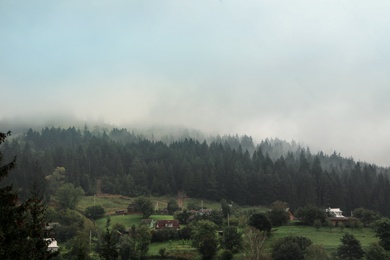 Photo of Picturesque landscape with small village and mountain forest covered in mist
